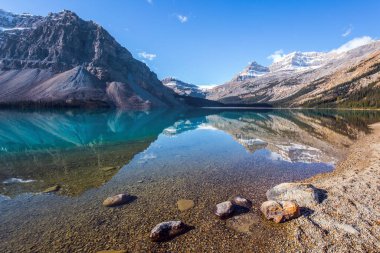 Kanada mı? Rocky Dağları. Dağlar gölün yumuşak suyuna yansıyor. Temiz gök mavisi suyu ile buzul gölü yayı. Güneşli bir sonbahar günü