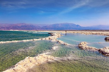 Ölü Deniz 'in İsrail kıyıları. Buharlaşmış tuz formları karmaşık desenler oluşturuyor. Ürdün kıyılarının pembe dağları. Rüzgarlı bir bahar günü. Siren bulutları mavi gökyüzünde uçar