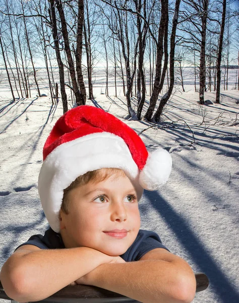 赤いサンタクロースの帽子のハンサムな男の子は勝利に笑顔 クリスマスが来る 冬の森の中で霜の多い雪の晴れた日 深い雪が地面を覆い — ストック写真