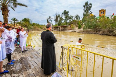 QASR El-YAHUD, ISRAEL - 2 Mart 2020: Vaftiz töreni. Vaftiz gömlekli adam Ürdün Nehri 'nin suyuna giriyor. İsa Mesih 'in vaftiz edildiği yer. Dini turizm kavramı