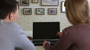 Genç masada oturan çift ve dizüstü ekran görünüyor.
