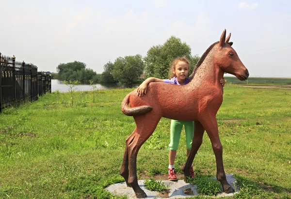 Little girl and sculpture foal. Tourist Complex Siberian Podvorye. — Stock Photo, Image