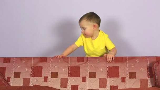 Glad glad liten pojke spelar och hoppa på soffan. — Stockvideo