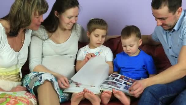 Eltern mit Kindern und Großmutter überlegen ein Album mit Fotos. glückliche Familie wartet auf drittes Kind. — Stockvideo