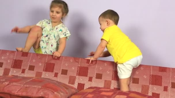 Šťastný radostné mladší bratr a sestra hraje a skákat na gauči. — Stock video