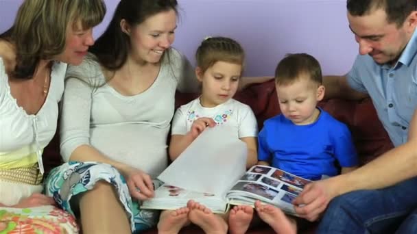 Eltern mit Kindern und Großmutter überlegen ein Album mit Fotos. glückliche Familie wartet auf drittes Kind. — Stockvideo