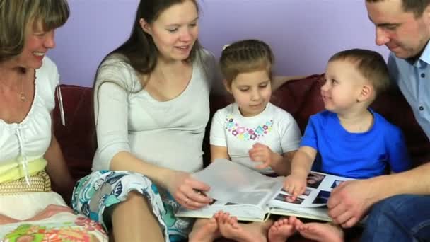 A szülők a gyerekek és a nagymama fontolja meg egy albumot a képek. Boldog család harmadik gyermeket vár. — Stock videók