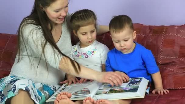 Μαμά με τα παιδιά θεωρούν ένα άλμπουμ με φωτογραφίες. Ευτυχισμένη οικογένεια σε αναμονή για το τρίτο παιδί. — Αρχείο Βίντεο