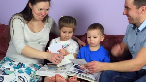 Батьки з дітьми розглядають альбом з фотографіями. Щаслива сім'я чекає третьої дитини . — стокове відео