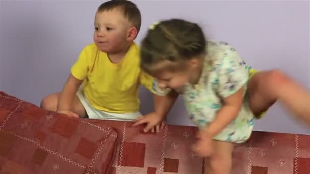 Happy joyful little brother and sister playing and jumping on couch. — Stock Video