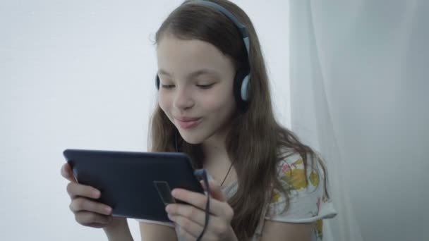 Beautiful little girl with headphones watching funny videos on tablet — Stock Video