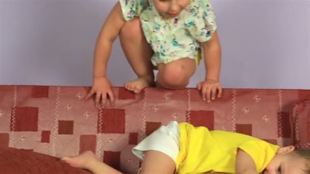 Щасливий радісний маленький брат і сестра грають і стрибають на дивані . — стокове відео