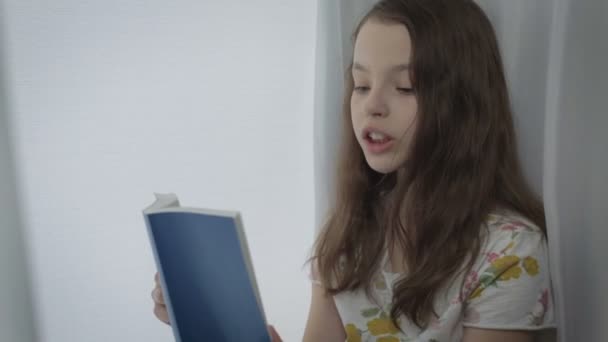 Beautiful little girl learns a poem by window. — Stock Video