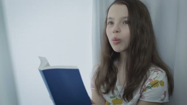 Beautiful little girl learns a poem by window. — Stock Video