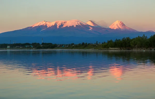 Solnedgång belysning Kluchevskaja grupp av vulkaner med reflektion i floden Kamchatka. — Stockfoto