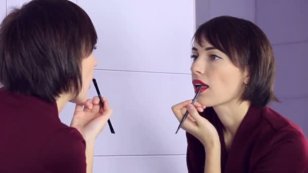 Beauty woman applying makeup. Beautiful girl looking in the mirror and paints her lips with brush. — Stock Video