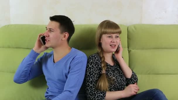 Young man and woman sitting on couch and talking on the smartphone. Lack of common interests. — Stock Video