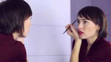 Güzellik kadını makyaj uygulamak. Güzel kız ayna ve boyalar kaşları fırça arıyorsunuz.