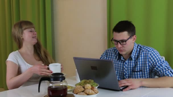 젊은 사람이 앉아서 노트북을 보고. 그는 바쁜 프로세스 이며, 그의 아내에 게 관심을 지불. 그녀는 아침 식사를 제공 하 고 그녀의 남편 부주의 원 망 해. — 비디오