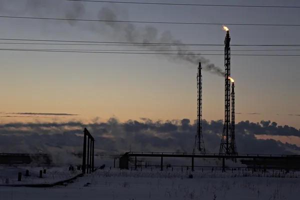 在落日的天空背景的炼油厂。雪人下雪的冬天的晚上. — 图库照片