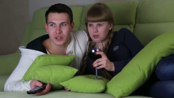 Verängstigtes junges Paar bei einem Glas Wein vor dem Fernseher. — Stockvideo