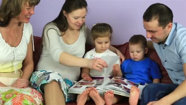 Los padres con niños y la abuela consideran un álbum con fotos. Familia feliz esperando al tercer hijo . — Vídeo de stock