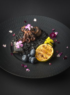 Risotto with octopus and blueberries on a black plate