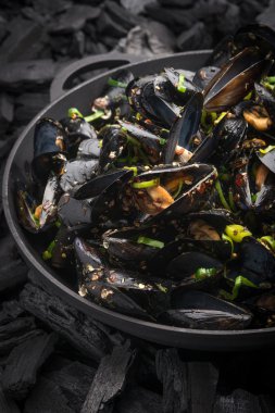 Steamed Mussels with vegetables in a black frying pan on the coa