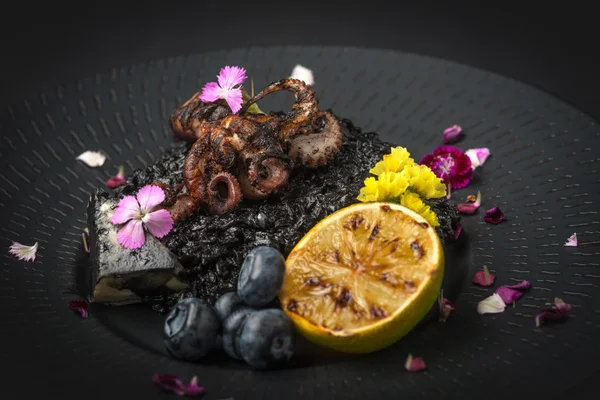 Risotto with octopus and blueberries on a black plate — ストック写真