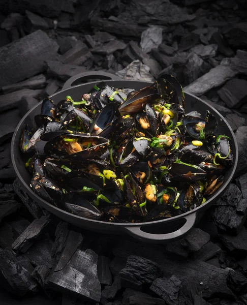 Steamed Mussels with vegetables in a black frying pan on the coa 图库照片