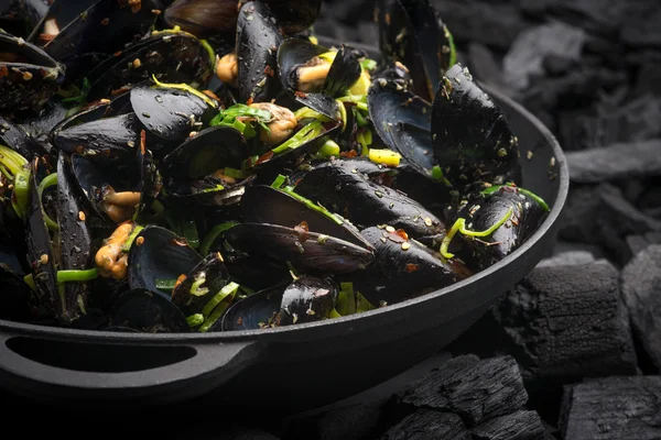 Steamed Mussels with vegetables in a black frying pan on the coa 免版税图库照片