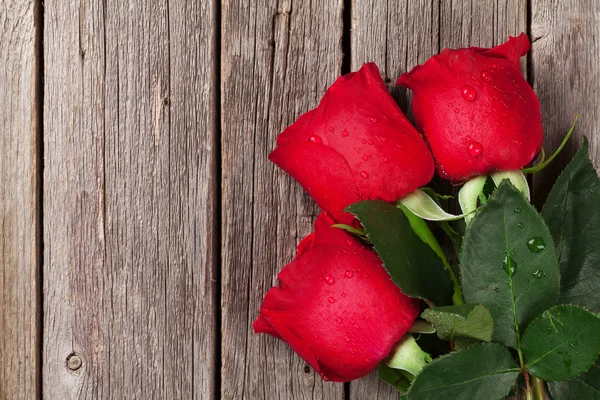 Rote Rosen über Holztisch — Stockfoto