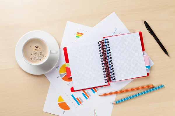 Posto di lavoro ufficio con caffè, blocco note e grafici — Foto Stock