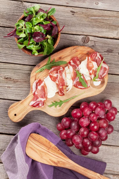 Prosciutto en mozzarella op bestuur en druiven — Stockfoto