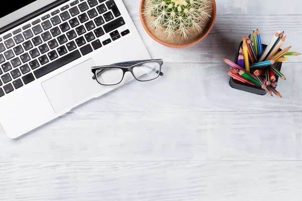 Skrivbord med laptop, glasögon och pennor — Stockfoto