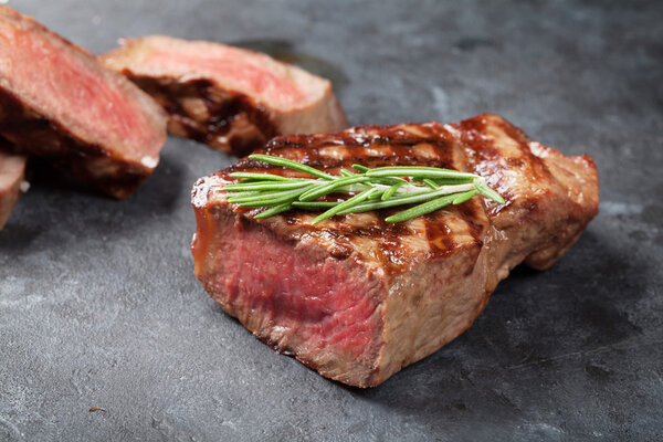 Grilled sliced beef steak with salt, pepper and rosemary on stone table