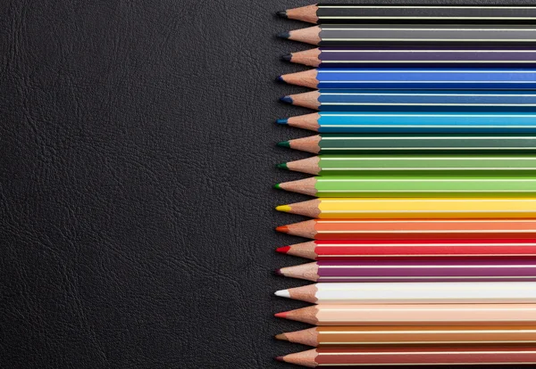 Colorful pencils over leather desk — Stock Photo, Image
