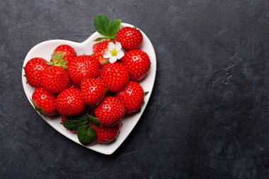 Taş masadaki kalp şeklinde kasede olgun bahçe çileği. Üst görünüm düzlüğü kopyalama alanı ile yatıyordu