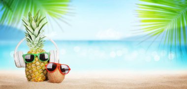 Parlak dalgalı tropikal deniz, güneş gözlüklü ananas ve sıcak kumsalda kulaklık. Kopya alanı ile seyahat ve tatil kavramı