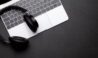 İş masası çalışma yeri ve ofis eşyaları siyah deri arka planda. Kulaklık ve dizüstü bilgisayar. Üstteki görünüm düzlüğü metin için kopyalama alanı ile yatıyordu