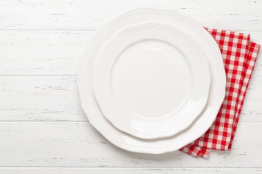 Beyaz boş tabak ve tahta masanın üzerine peçete. Üst görünüm düz, yemek için yer var.