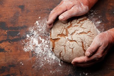 Baker, ahşap masada taze ev yapımı ekmeği tutuyor. Üst görünüm düzlüğü kopyalama alanı ile yatıyordu
