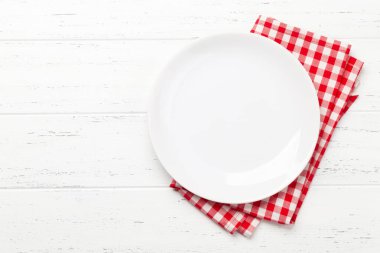 Beyaz boş tabak ve tahta masanın üzerine peçete. Üst görünüm düz, yemek için yer var.