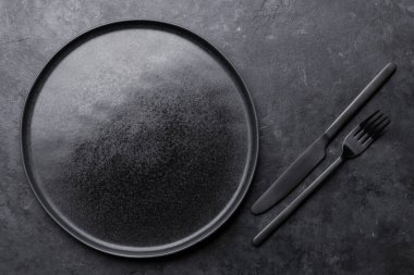 Boş tabak, çatal ve bıçaklı mutfak masası. Pişirme taşı arka planı. Kopyalama alanı olan üst görünüm. Düz yatıyordu