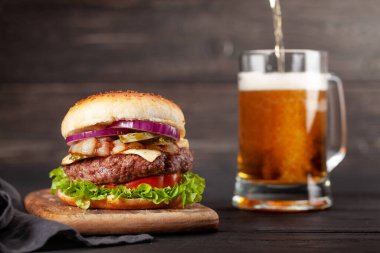 Büyük sığır eti, peynir, domates, pastırma, marul ve bira bardağıyla ev yapımı lezzetli hamburger. Kopyalama alanı ile