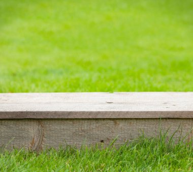 Boş ahşap masa ve bahçedeki çimen bokeh. Ürününüzü göstermek için şablon arkaplanı