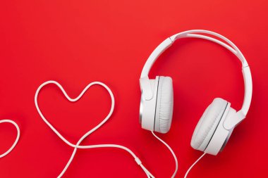 Kulaklık ve kalp şeklindeki kablo kırmızı fonun üzerinde. Aşk müziği ya da Sevgililer Günü konsepti. Üst görünüm düzlüğü kopyalama alanı ile yatıyordu