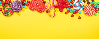 Çeşitli tatlı çeşitleri var. Şeker, bonbon ve sarı arka planda badem kurabiyesi. Üst görünüm düzlüğü kopyalama alanı ile yatıyordu