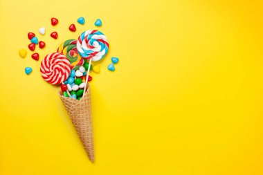 Çeşitli tatlı çeşitleri var. Şeker, bonbon ve dondurma külahında lolipop, sarı arka planda. Üst görünüm düzlüğü kopyalama alanı ile yatıyordu