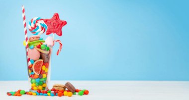 Çeşitli tatlı çeşitleri var. Şeker, bonbon, çikolata ve mavi arka planda kokteyl bardağında kurabiye. Kopyalama alanı ile